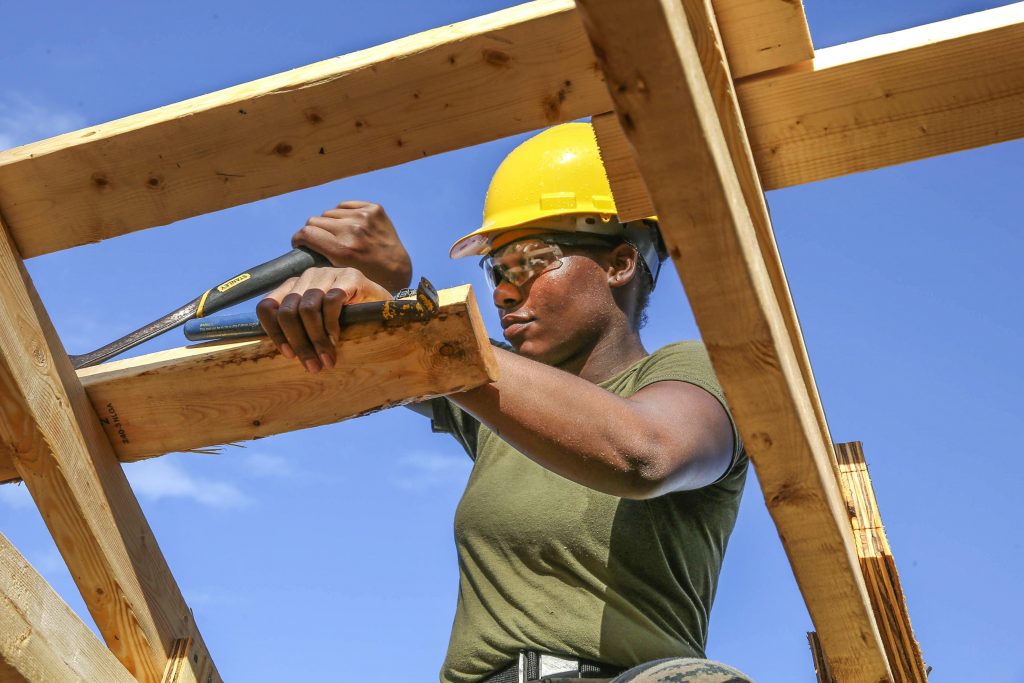 African American woman wearing green shirt and yellow construction hat working with tools on carpentry project.